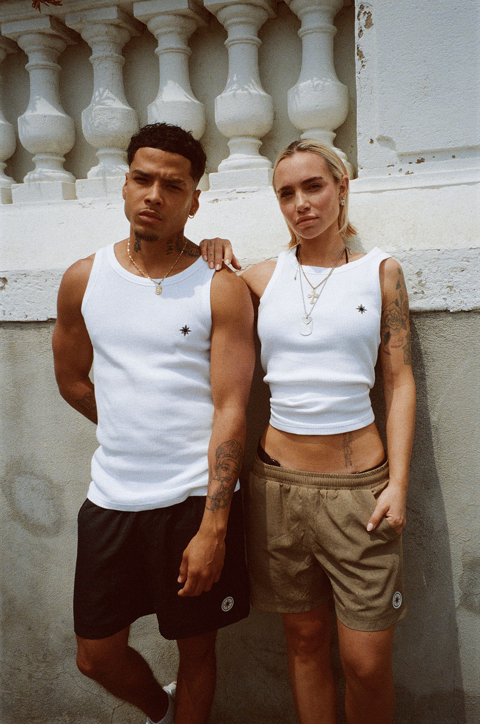 Femme et homme adossés à un mur, tous deux en Swim Shorts et Tank Top Finesse.