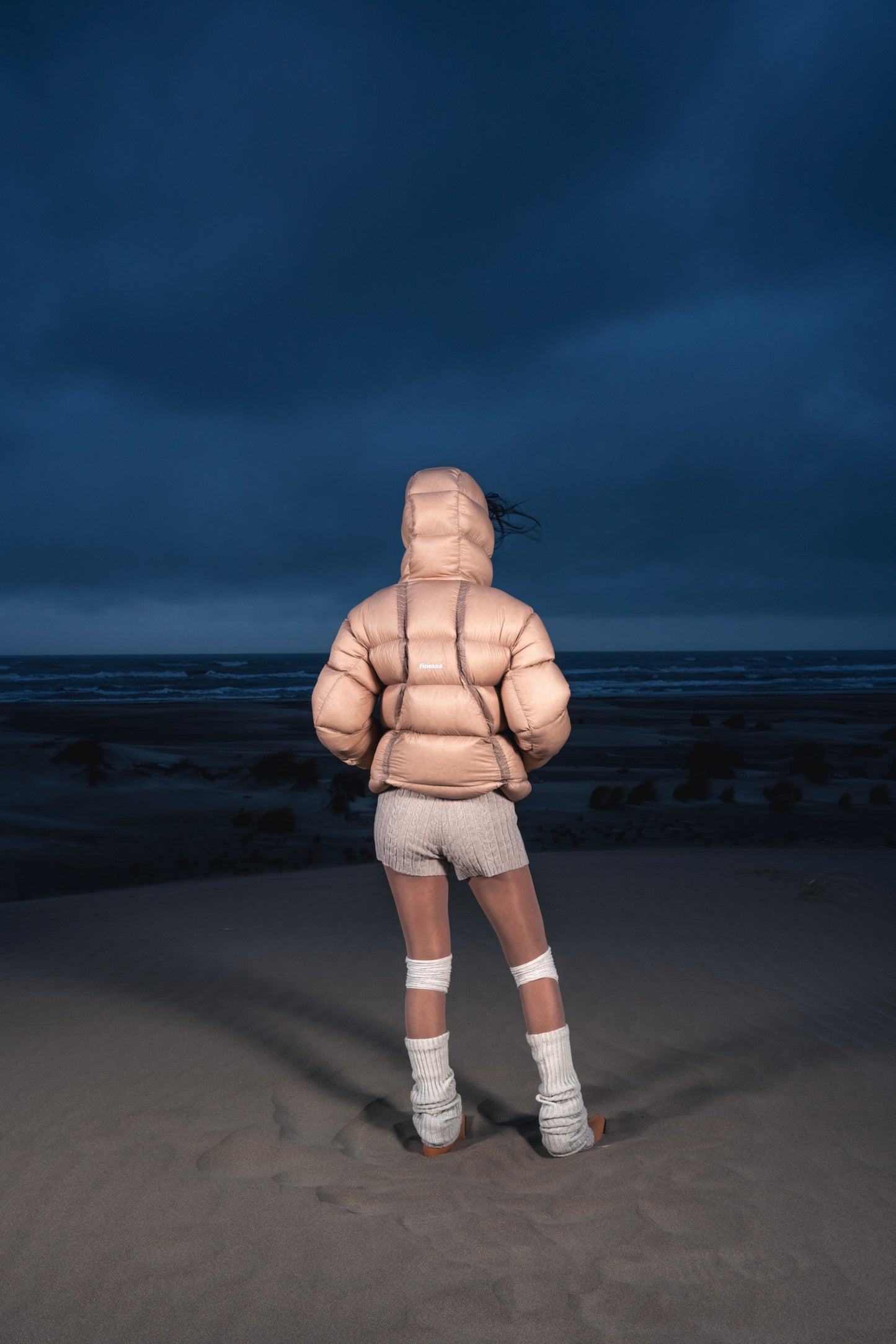Femme de dos dans les dunes portant la Finesse Alive Puffer Jacket beige