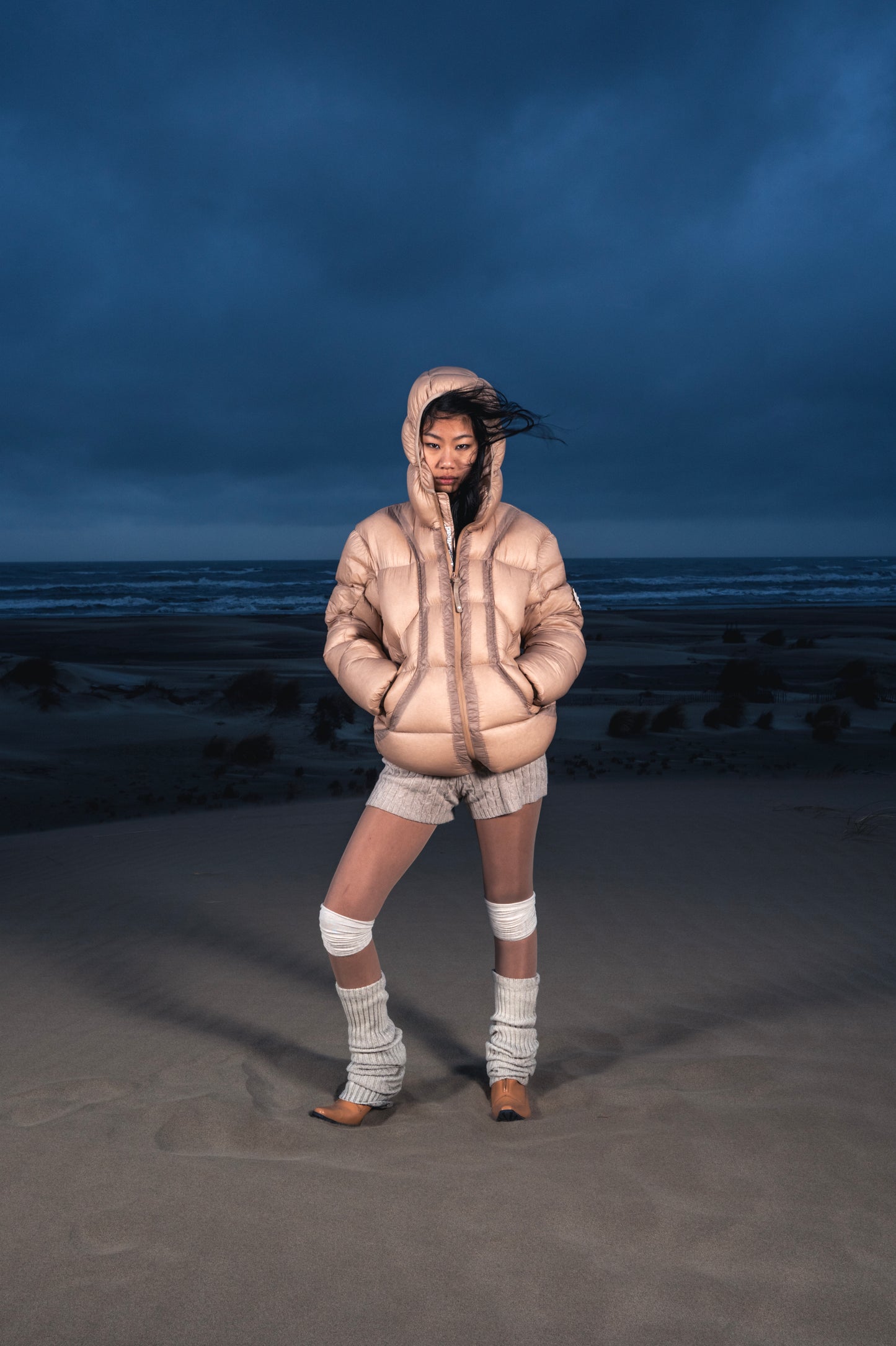Femme de face dans les dunes portant la Finesse Alive Puffer Jacket beige.