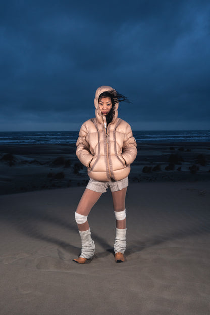 Femme de face dans les dunes portant la Finesse Alive Puffer Jacket beige.