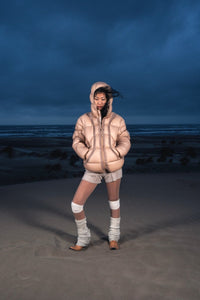 Femme de face dans les dunes portant la Finesse Alive Puffer Jacket beige.
