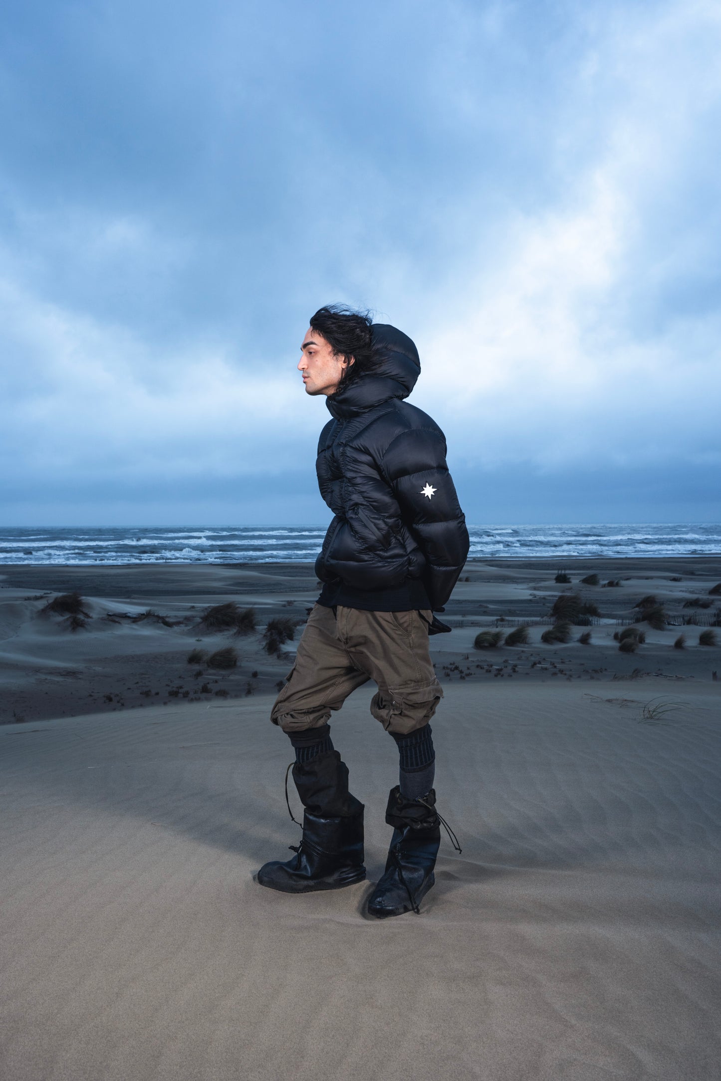 Homme de face dans les dunes, regard à droite, en Alive Puffer Jacket.