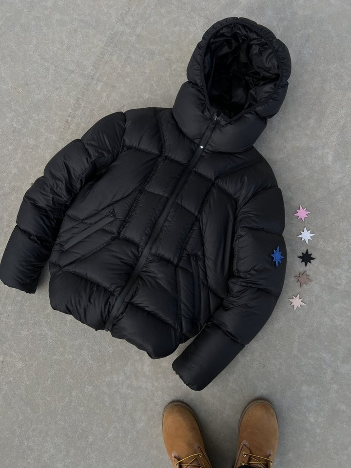 Doudoune Alive Puffer Jacket noire posée au sol, avec Timberlands visibles.