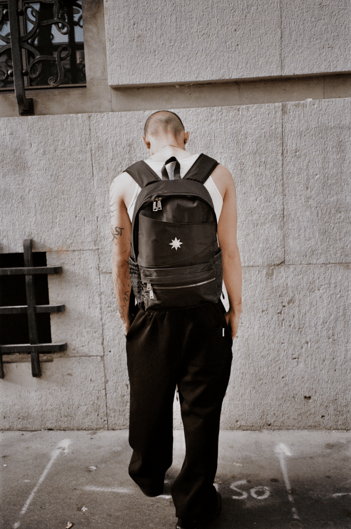 Homme vu de dos devant mur urbain portant le Finesse Black Vanta Backpack.