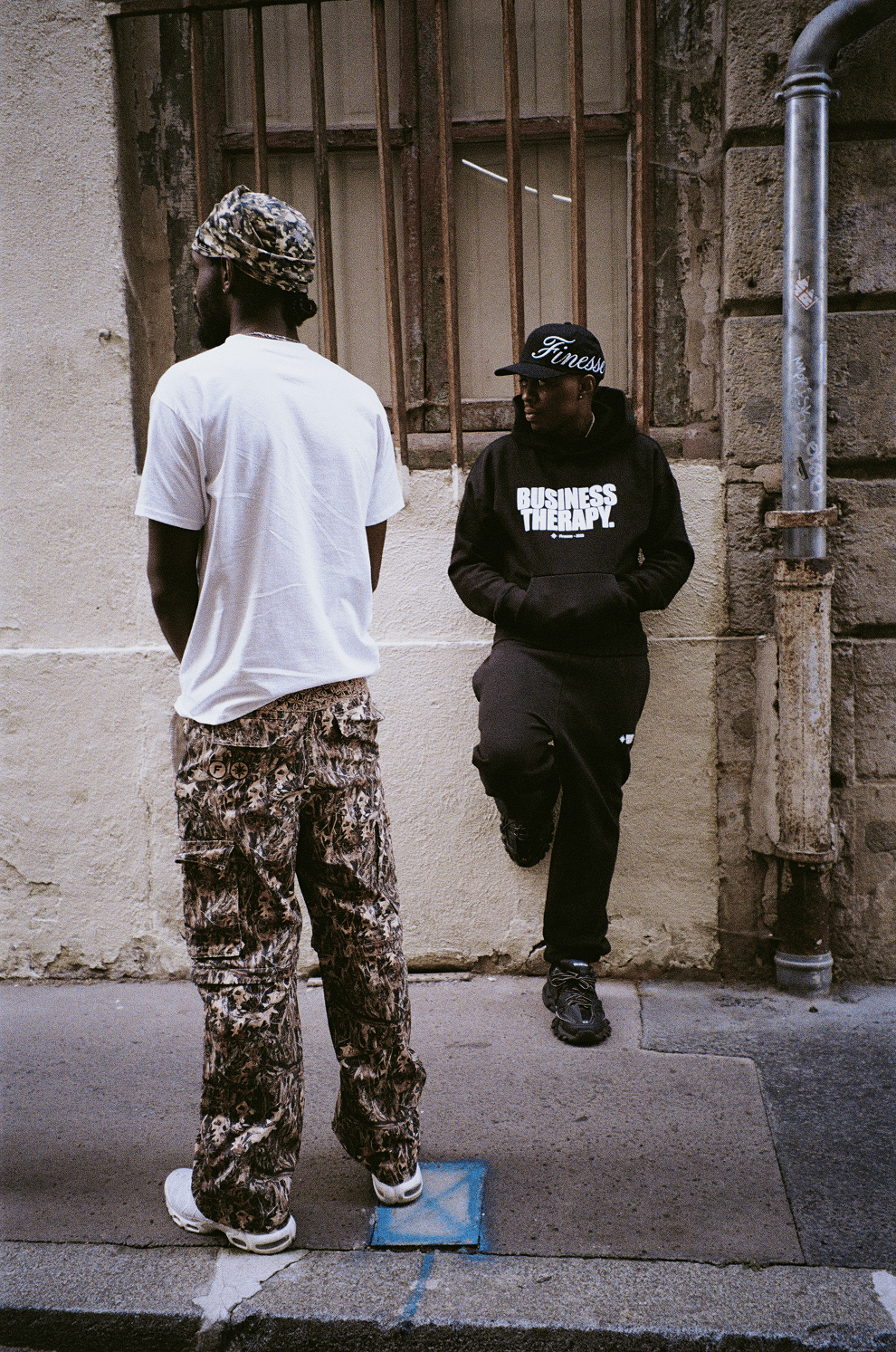 Homme de dos en 2-in-1 Cargo Pants, second mannequin en Business Therapy noir avec Finesse "SIGN" Cap Black.