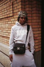 "Homme en jogging gris Business Therapy avec Memorial Bag, au coin d’une rue devant mur de briques