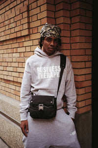 "Homme en jogging gris Business Therapy avec Memorial Bag, au coin d’une rue devant mur de briques