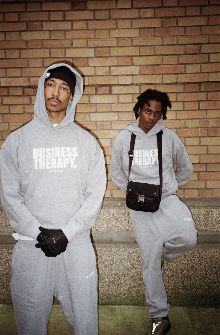 Deux hommes en jogging gris Business Therapy devant mur de briques, un avec Memorial Bag.