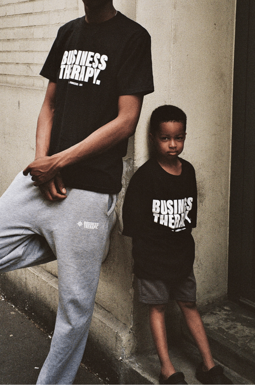 Enfant adossé à un adulte dans un décor urbain, tous deux portant un t-shirt Business Therapy.