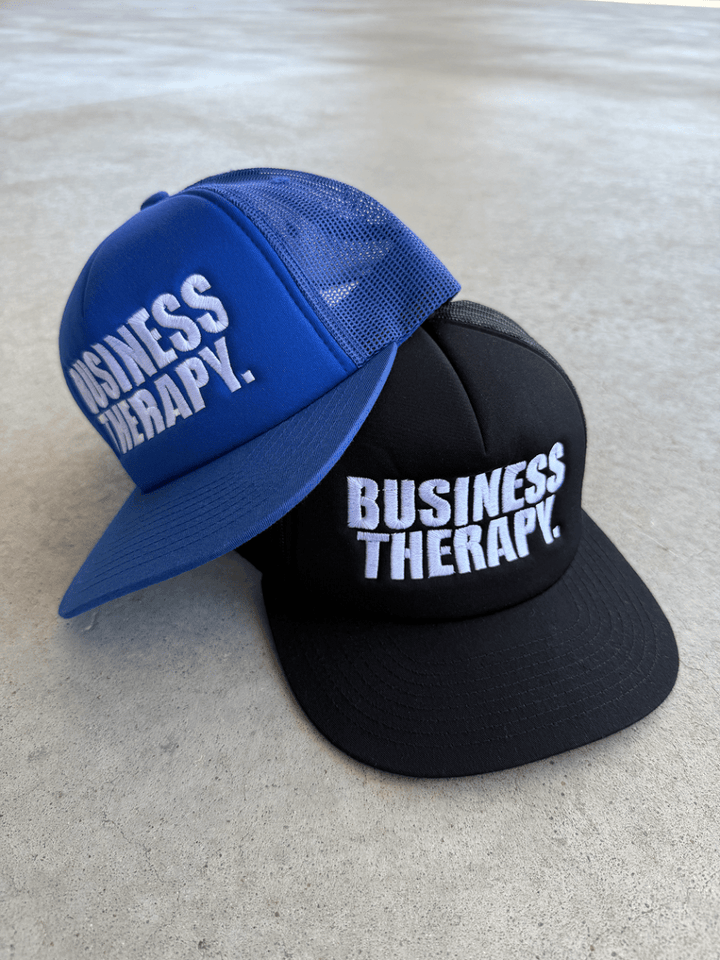 Casquettes Business Therapy Trucker bleue et noire posées au sol en packshot.