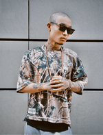 Homme tatoué en Jersey 44 camo, lunettes Sunglasses Series 01, mains jointes.