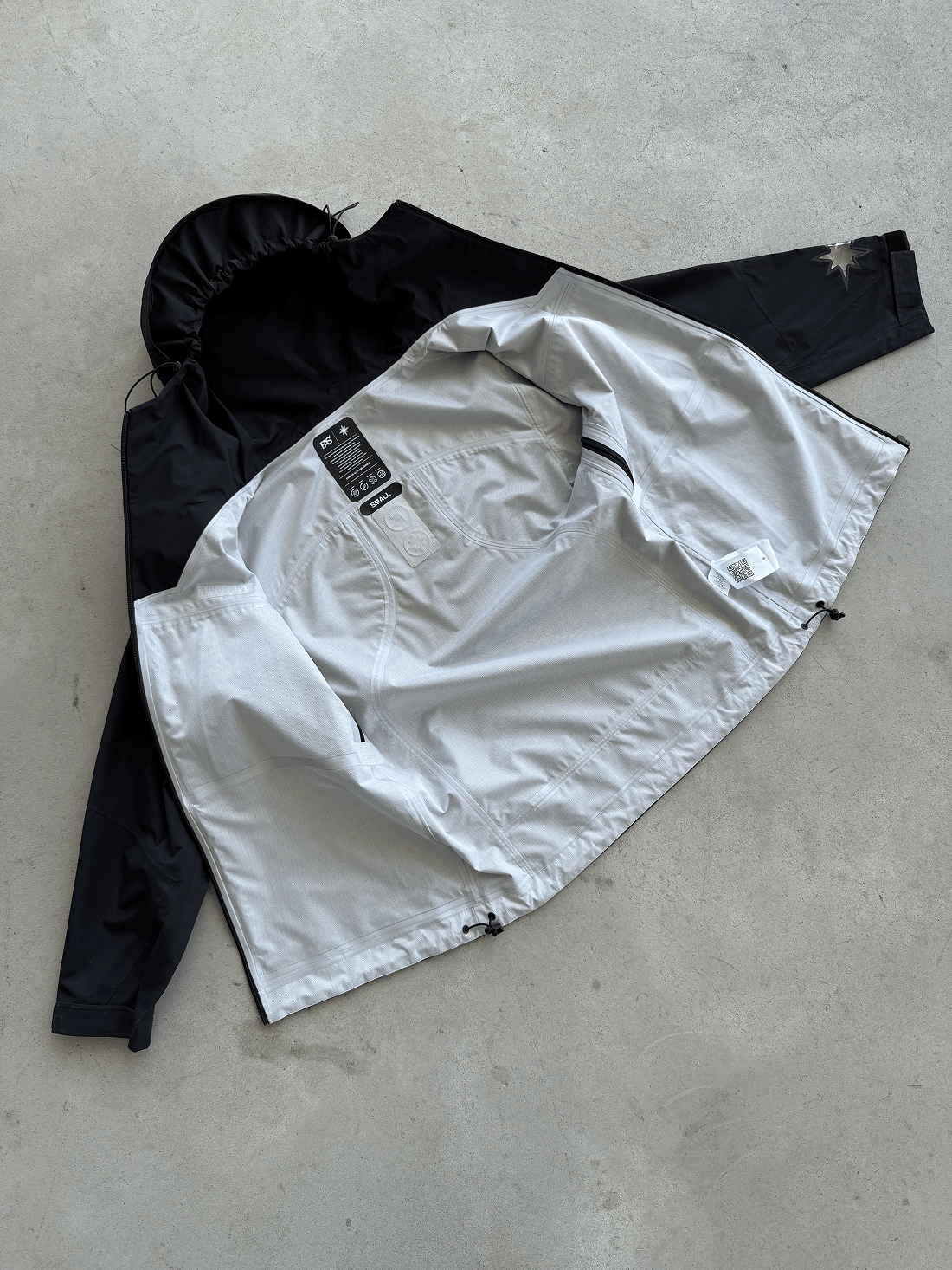 FAS Hardshell noire posée ouverte au sol, capuche et intérieur visibles