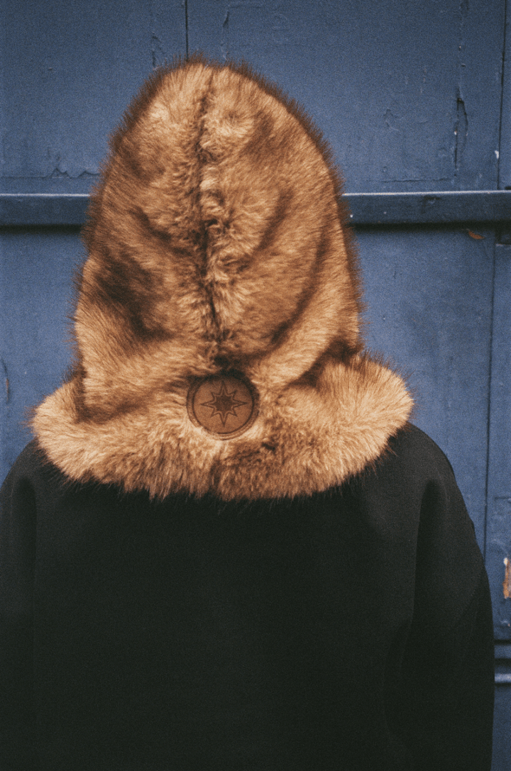 Personne de dos devant une porte bleue, capuche FUR HOOD visible avec patch cuir
