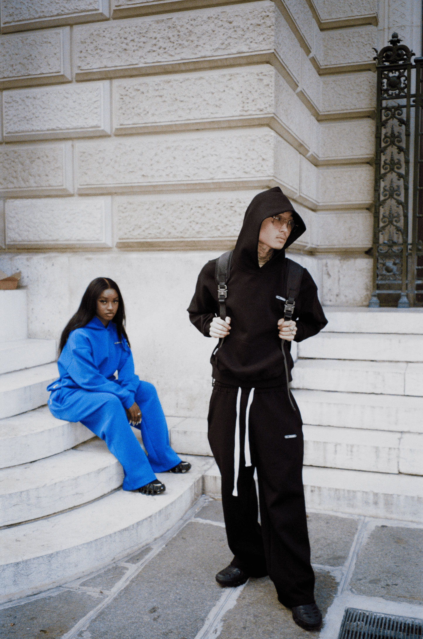 Deux mannequins : femme assise en arrière-plan en ensemble Air Cotton bleu, homme en avant-plan en ensemble noir.