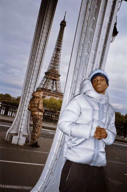 Photo argentique d’un homme portant la Finesse* Alive Puffer Jacket Ice Blue sur un pont à Paris.