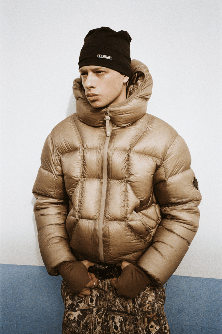 Mannequin portant la doudoune Finesse* Alive Puffer Jacket Light Bronze et le Finest Skull Cap Beanie sur un fond texturé.