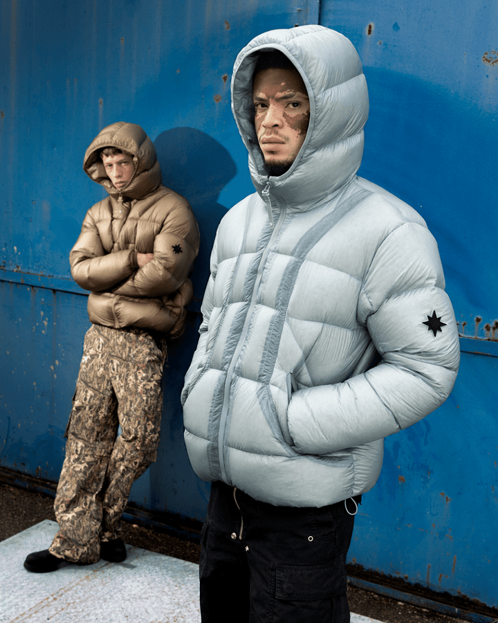 Deux mannequins portant les doudounes Finesse* Alive Puffer Jacket Ice Blue et Light Bronze devant un mur bleu.