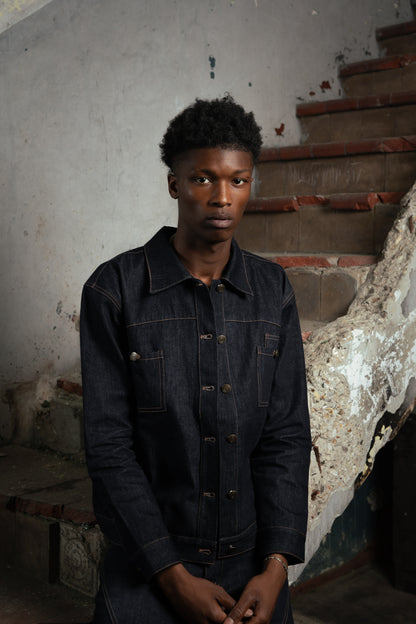 Homme posant dans un bâtiment abandonné, portant la Finesse Denim Jacket ouverte près d’un escalier.