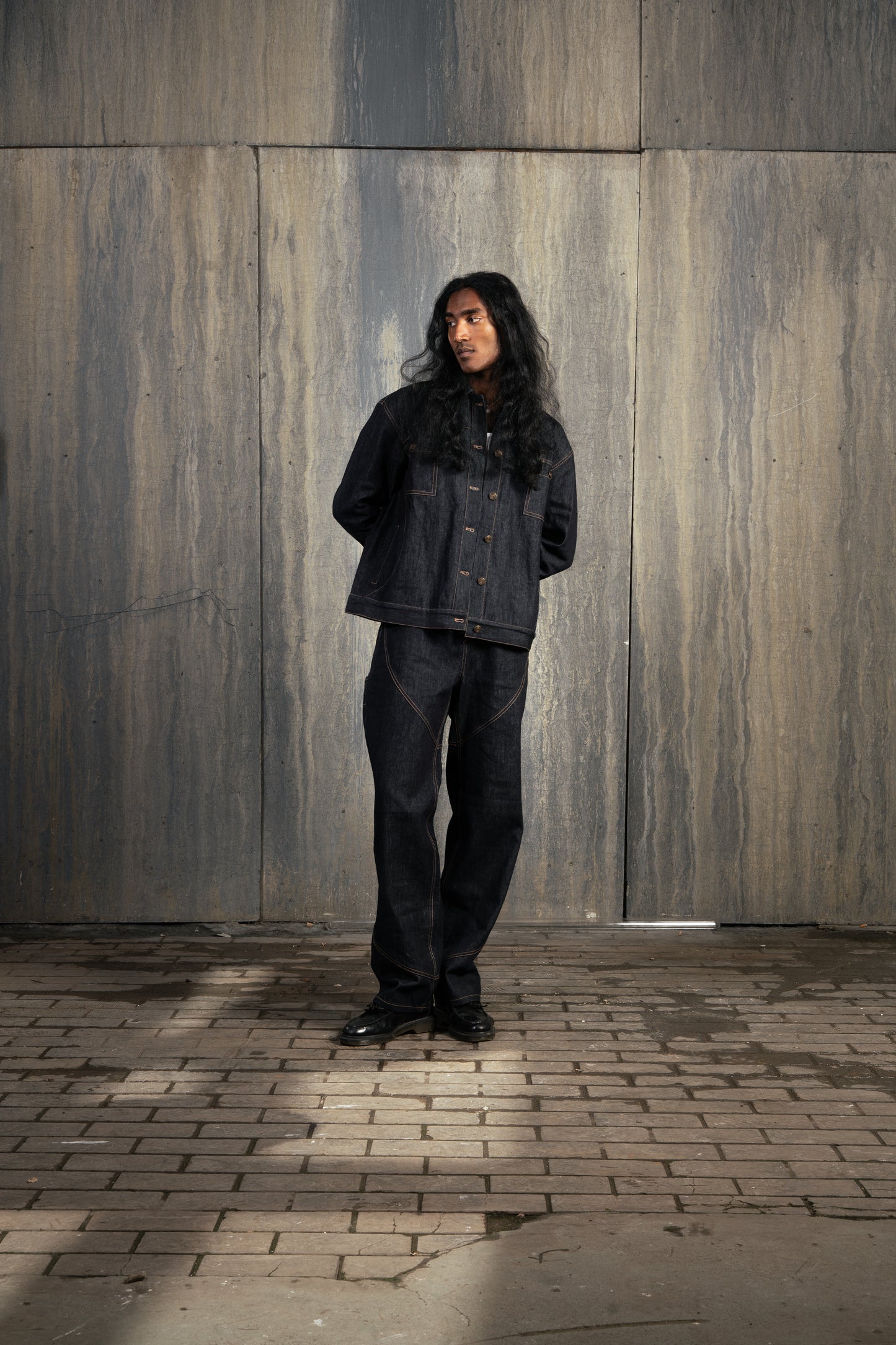 Homme de face en studio à décor industriel, bras derrière le dos, portant l’ensemble Finesse Denim Set ADV