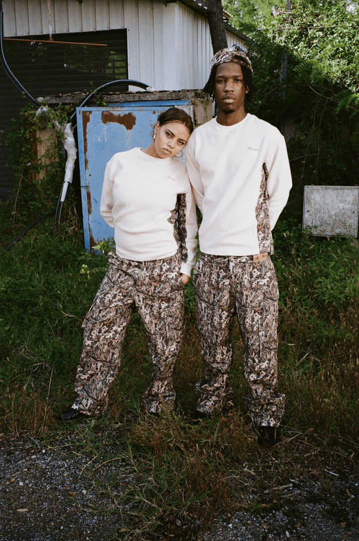 Homme et femme enlacés devant un garage, en Finesse Military Top-Camo et 2-in-1 Cargo Pants-Camo.
