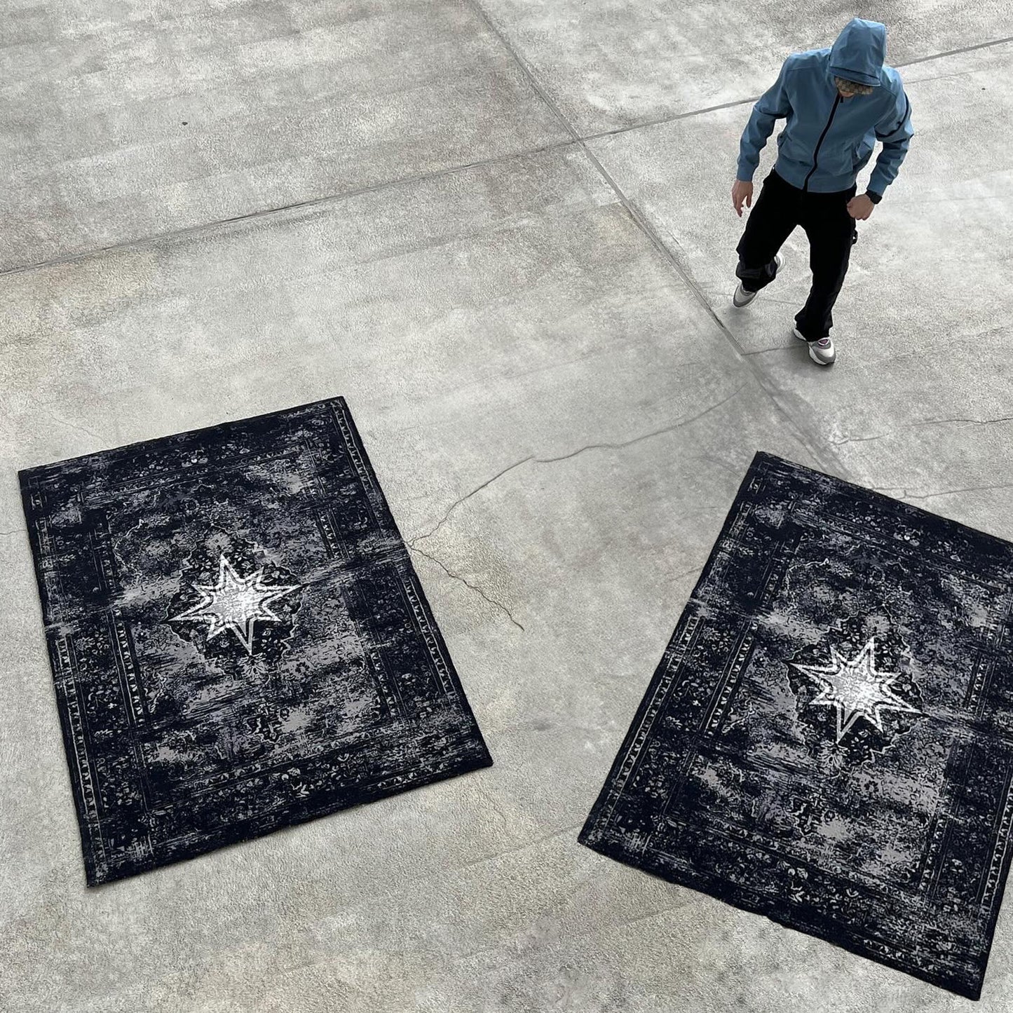 Vue plongeante dans un hangar au sol en béton, avec deux Finesse Rugs et un homme en veste bleue.