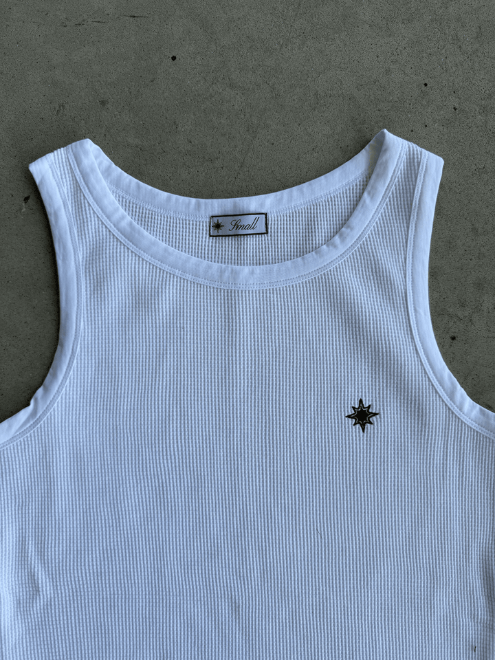 Zoom sur logo pec du Tank Top Finesse blanc posé au sol.