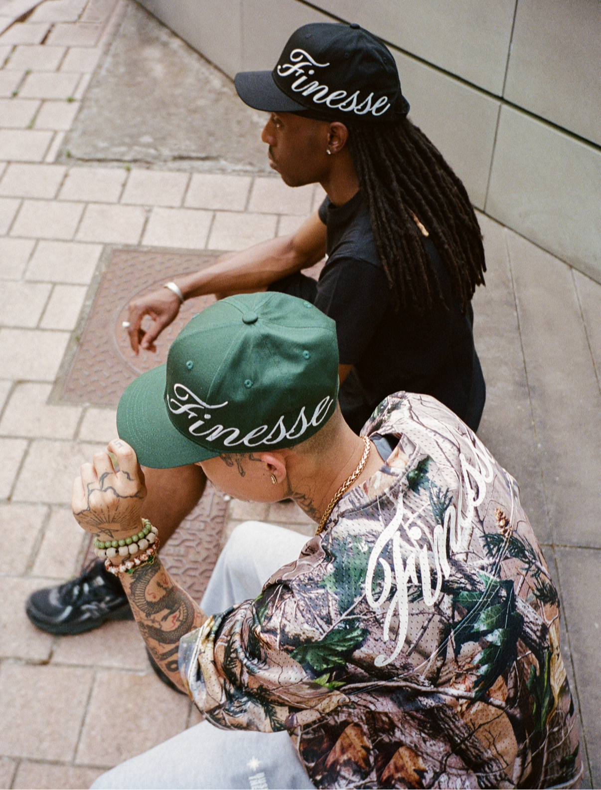 Deux hommes assis dans la rue en Jersey 44 camo et black, casquettes Sign Cap verte et noire.